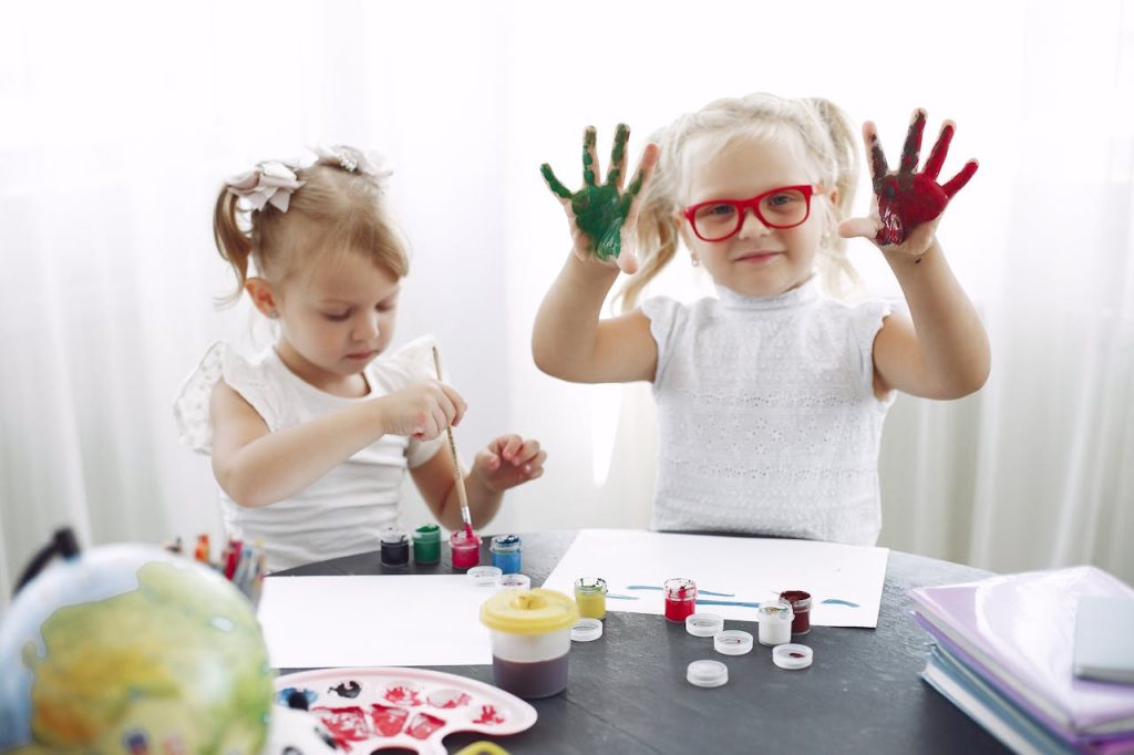 Small girls with braids in white tee shirts have drawing class in kindergarten